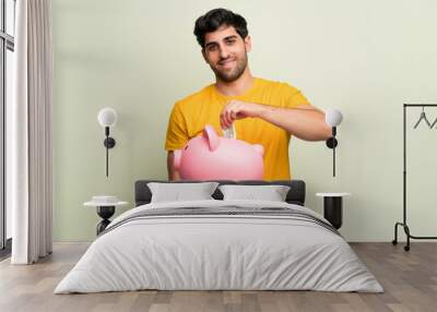 Young man over pink wall taking a piggy bank and happy because it is full Wall mural