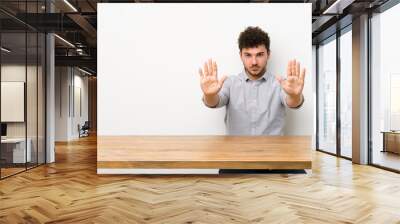 Young man with a table making stop gesture and disappointed Wall mural