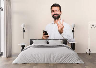 Young man with beard holding a mobile happy and counting three with fingers Wall mural