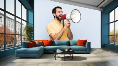 Young man with beard over isolated blue background shouting through a megaphone Wall mural