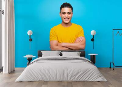 Young man with yellow shirt over isolated blue background keeping the arms crossed in frontal position Wall mural