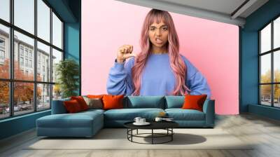 Young mixed race woman with pink hair isolated on pink background showing thumb down with negative expression Wall mural