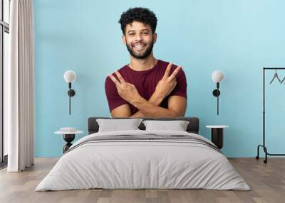 Young Moroccan man isolated on blue background smiling and showing victory sign Wall mural