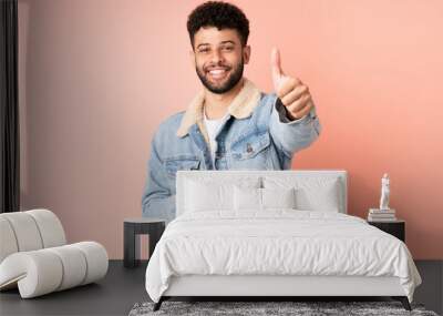 Young Moroccan man using mobile phone isolated on pink background with thumbs up because something good has happened Wall mural