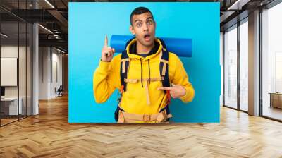 Young mountaineer man with a big backpack over isolated blue background with surprise facial expression Wall mural