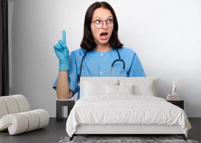 Young nurse caucasian woman isolated on white background intending to realizes the solution while lifting a finger up Wall mural