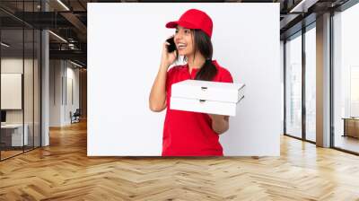 Young Pizza delivery girl over isolated white background keeping a conversation with the mobile phone Wall mural