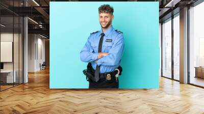 Young police blonde man isolated white on blue background with arms crossed and looking forward Wall mural