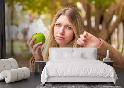 Young pretty blonde woman with an apple at outdoors Wall mural