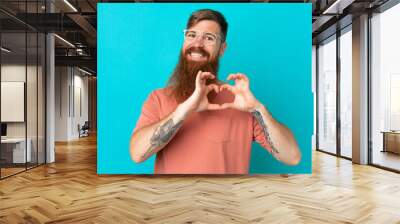 Young reddish caucasian man isolated on blue background With glasses making heart with hands Wall mural