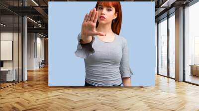 Young redhead girl making stop gesture with her hand on blue background Wall mural