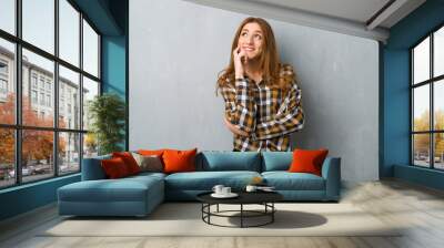 Young redhead girl over grunge wall thinking an idea while looking up Wall mural