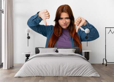 Young redhead woman isolated on white background showing thumb down with two hands Wall mural