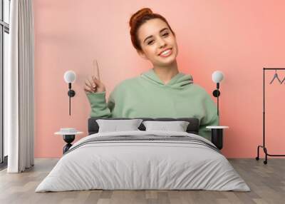 Young redhead woman with sweatshirt showing and lifting a finger in sign of the best Wall mural