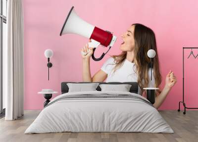 Young Romanian woman isolated on pink background shouting through a megaphone to announce something in lateral position Wall mural