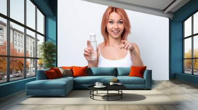 Young Russian girl with a bottle of water isolated on white background surprised and pointing front Wall mural