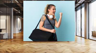 Young sport Brazilian woman with sport bag isolated on blue background celebrating a victory Wall mural