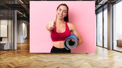 Young sport caucasian woman going to yoga classes while holding a mat isolated on pink background showing and lifting a finger Wall mural