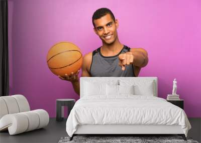 Young sport man with ball of basketball over isolated purple wall points finger at you with a confident expression Wall mural