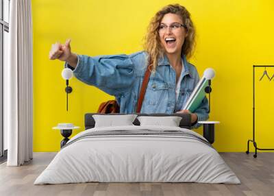 Young student caucasian woman isolated on yellow background giving a thumbs up gesture Wall mural