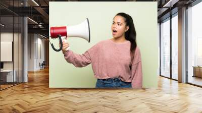 Young teenager Asian girl over isolated green background holding a megaphone Wall mural