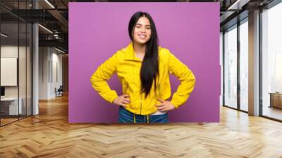 Young teenager Asian girl over isolated purple background posing with arms at hip and smiling Wall mural