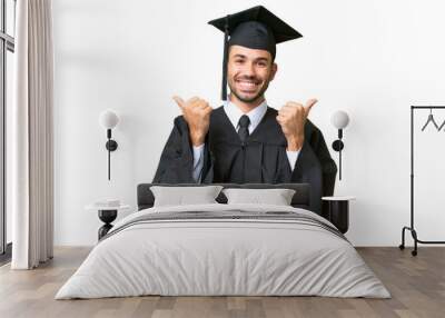 Young university graduate man over isolated background with thumbs up gesture and smiling Wall mural