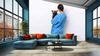 Young veterinarian woman with dog on a table isolated on white background in back position Wall mural