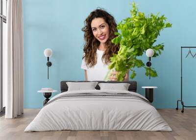 Young woman holding a celery isolated on blue background with happy expression Wall mural