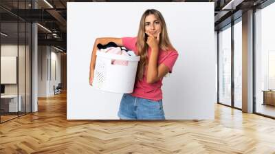 Young woman holding a clothes basket isolated on white background thinking Wall mural