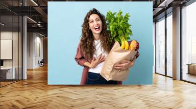 Young woman holding a grocery shopping bag isolated on blue background smiling a lot Wall mural