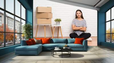 Young woman moving in new home among boxes keeping arms crossed Wall mural