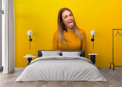 Young woman on yellow background showing tongue at the camera having funny look Wall mural