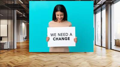 Young woman over isolated background holding a placard with text We Need a Change Wall mural