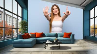 Young woman over isolated blue background counting seven with fingers Wall mural