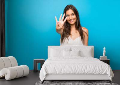 Young woman over isolated blue background happy and counting four with fingers Wall mural