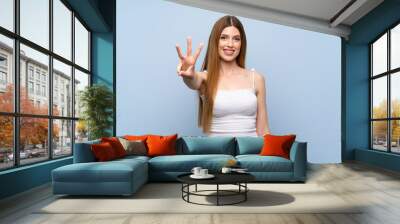 Young woman over isolated blue background happy and counting three with fingers Wall mural