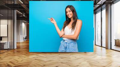 Young woman over isolated blue background pointing finger to the side Wall mural