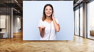 Young woman over isolated blue background working with headset Wall mural