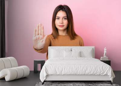 Young woman over isolated pink background making stop gesture Wall mural