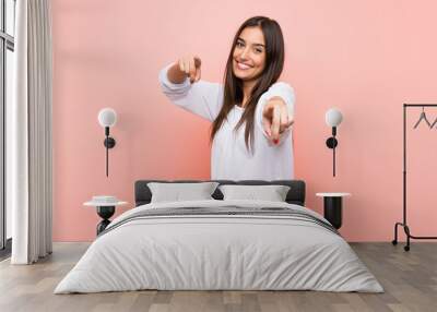 Young woman over isolated pink background points finger at you while smiling Wall mural