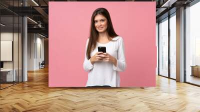 Young woman over isolated pink background sending a message with the mobile Wall mural