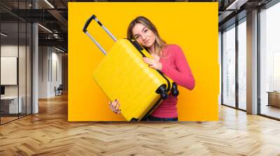 Young woman over isolated yellow background in vacation with travel suitcase Wall mural