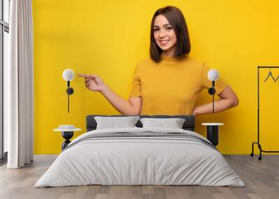 Young woman over yellow wall pointing finger to the side Wall mural