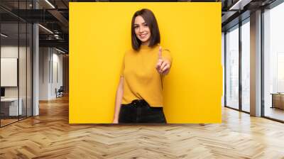 Young woman over yellow wall showing and lifting a finger Wall mural