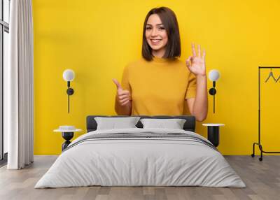 Young woman over yellow wall showing ok sign with and giving a thumb up gesture Wall mural