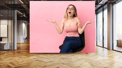 Young woman sitting on a chair over isolated pink background with shocked facial expression Wall mural