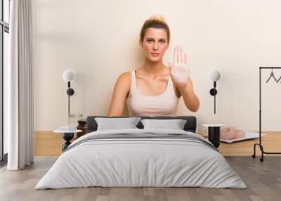 Young woman with lots of different mini cakes in a table making stop gesture with her hand Wall mural