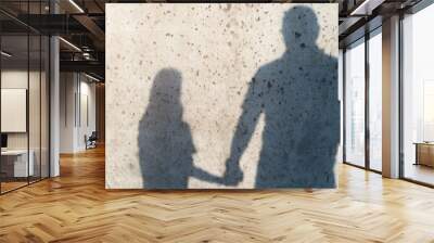 Two silhouettes, men and girl, shadows on the wall. Father holds daughter by the hand. Reflection on a concrete wall on a sunny day. The concept of family, understanding between father and daughter Wall mural