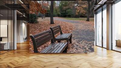 A photograph of two wooden benches placed on an autumn park path, surrounded by fallen leaves in shades of orange and brown Wall mural